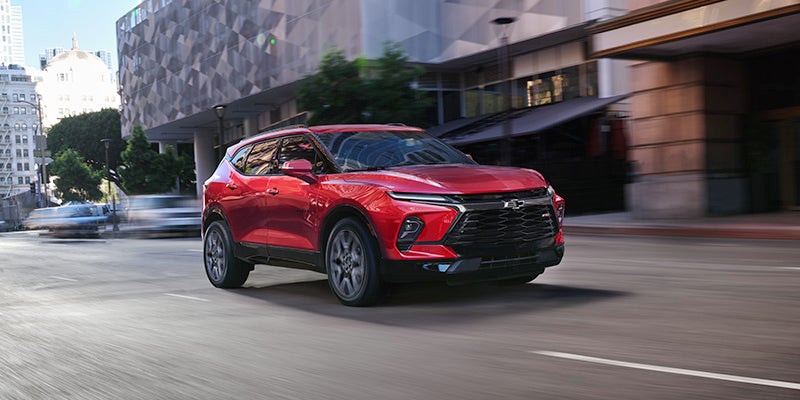 A 2024 Chevrolet Blazer driving along a bustling city street, showcasing its sleek design and urban environment.