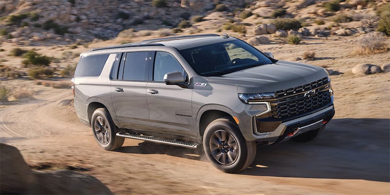 A 2024 Chevrolet Suburban parked on a dirt road, showcasing its rugged design and off-road capabilities.