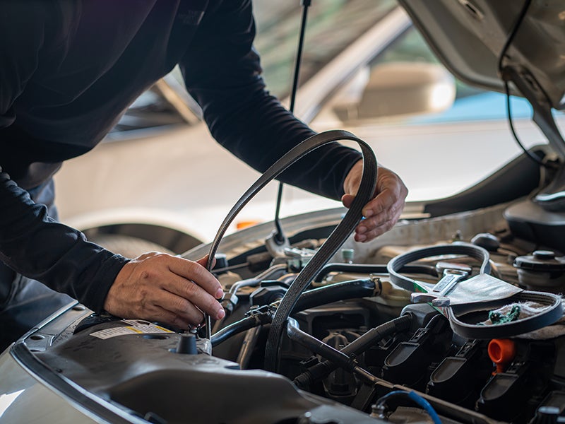 A man repairs a car engine, focused on the mechanical components and tools around him in a garage setting.